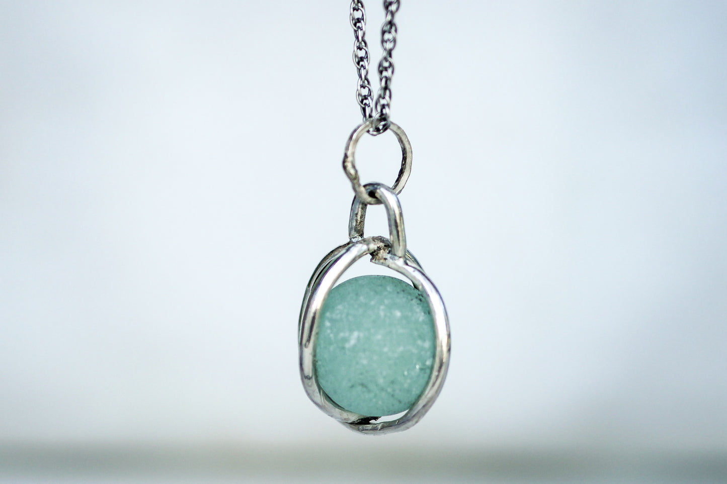 Victorian Codd sea glass marble pendant shown rotating inside silver cage, ocean inspired necklace